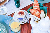 Ein eleganter Brunch-Tisch mit Cappuccino, Croissants, Brot und Orangensaft vor einem beruhigenden Hintergrund
