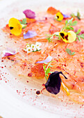 From above close up shot of appetizing carpaccio with herbs and flowers served on white plate