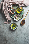Gesunde Kochzutaten auf grauem Betonküchentisch: Olivenöl, Salbei, Knoblauch, Pfeffer, Salz, Kochlöffel aus Holz, Geschirrtuch. Kochen von schmackhaftem Essen zu Hause. Ansicht von oben