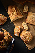 From above high angle of delicious freshly baked bread with crispy crust sprinkled with mix of seeds and placed on wooden cutting board