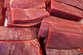 Closeup view of freshly cut pieces of raw red meat stack together over surface in bright kitchen