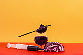 Composition of glass with strainer and syringe filled with homemade juice of red cabbage against bright background