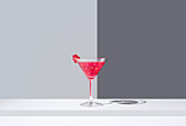 Glas mit rotem Granatapfelcocktail und Granatapfelkernen vor einem grauen Hintergrund, der einen weichen Schatten wirft