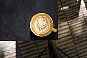 Draufsicht auf einen Keramikbecher mit frischem aromatischem Milchkaffee auf einem schwarzen Esstisch im Tageslicht