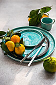 A striking composition featuring ripe tangerine with leaves on an aqua-hued ceramic plate, adding a touch of natural freshness.