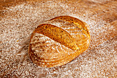 Nahaufnahme eines frisch gebackenen, leckeren Brotes mit knuspriger Kruste auf einem Holztisch mit Mehl rundherum in der Küche einer Bäckerei