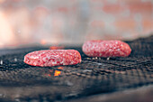 Two raw hamburger patties cook on a grill over glowing coals, capturing the essence of barbecue