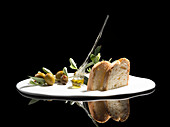 Exquisite bread toasts served on white plate with green herbs and olives with oil against against black background