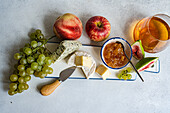 From above assorted yummy snacks with different types of cheese and sweet served on ceramics plate with grapes apple and figs on table