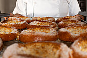 Crop anonymous female baker in white uniform standing by counter while preparing delicious baked bread with cheese in bakery