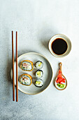 From above of japanese food set with avocado maki roll and fried sushi with soy sauce and ginger placed on a white concrete table