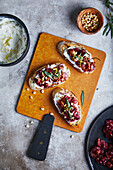 Draufsicht auf appetitlichen Ricotta-Toast mit gerösteten Trauben und Zitronenschale, serviert mit Estragon und Pinienkernen auf knusprigem Brot auf Holzbrett auf grauem Tisch