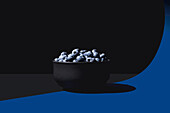 A minimalist composition featuring a black bowl of blueberries on a split blue and black background with dramatic lighting