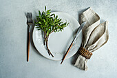 Draufsicht auf eine Tischdekoration mit frischen Pistazien auf einem Teller mit Besteck neben einer Serviette auf einer grauen Fläche bei Tageslicht