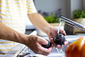 Seitenansicht einer anonymen männlichen Person, die Avocados mit Wasser aus dem Wasserhahn in der Küchenspüle wäscht, während sie kocht, mit unscharfem Hintergrund