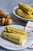 Ripe sweet corns served on plates near napkin on gray table