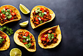Top view of many tacos filled with chopped tomatoes over meat with chickpeas and cilantro on top served on black background. Generative AI