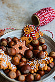 Teller mit einem Haufen Maronen und leckeren Weihnachtsplätzchen auf dem Tisch neben einer Spule mit rotem Faden