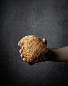 Hand of crop anonymous person holding fresh backed aromatic bread with crispy crust on grey background