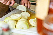 Close-up of an anonymous chef's hands slicing onions, with the focus on the onion layers and the knife's edge, set against a soft-focus kitchen background