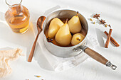 From above saucepan with delicious poached pears in white wine at table near star anise and jar with juice