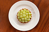 Top view of appetizing matcha cake dessert with green cream on white plate over wooden dining table in daylight