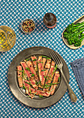 From above delicious sliced roast beef tagliatta served on plate near bowl with broccoli and herbs placed on patterned table towel