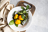 Fresh tangerines on a classic white plate over a textured beige napkin, conveying rustic charm and simplicity.