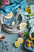 From above decorated table with various dishware and silverware with fresh slices of lemon placed on blue concrete background near napkin and cutlery with flower bouquet