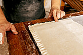 Hand eines nicht erkennbaren männlichen Bäckers, der beim Backen von leckerem Gebäck in einer Backstube durch Drücken der Ränder Muster auf gefüllten rohen Teig zeichnet