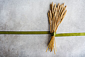 Top view of wheat ears bouquet with green ribbon placed on gray table