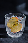 Tonic water with an apple slice in a glass set against a dark, moody background with dramatic lighting