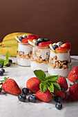 Yogurt whit fresh strawberries and blueberries with sliced banana placed in cups and on white marble table bright room