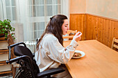 Content woman in a wheelchair enjoys a homemade meal at a dining table, exemplifying accessibility at home