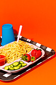 From above of spaghetti with tomato sauce fresh cucumber slices and strawberries with empty glass for water served for school lunch