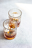 Hoher Winkel von Whiskeygläsern mit Eis und Orangenschalen auf grauem Hintergrund