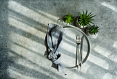 Top view of minimalist table setting with small potted plants near plate with cutlery and napkin in sunlight