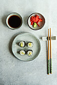 From above of japanese food set with avocado maki roll and fried sushi with soy sauce and ginger placed on a white concrete table