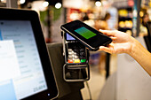 Unrecognizable person in supermarket and paying with credit card using mobile phone at self-service checkout