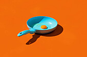 Whole raw egg yolk placed in blue frying pan with handle isolated against orange background