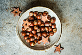 From above of plate of heap of chestnuts with tasty Christmas cookies placed on table in concrete grey background