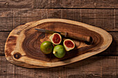 A rustic scene of fresh green figs, one sliced open, on an oval wooden cutting board alongside a vintage knife.