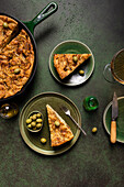 Draufsicht auf eine Scheibe gebackenes italienisches Focaccia-Brot mit grünen Oliven in einem Teller auf einem Esstisch mit Getränk auf grünem Hintergrund