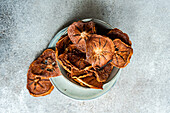Top view of slices of dried apples served in ceramic bowl on plate against blurred gray background