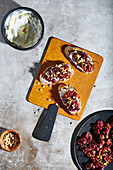 Top view of appetizing ricotta toast with roasted grapes and lemon zest served with tarragon and pine nuts placed on crusty bread on wooden board on gray table