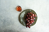 Top view of red Champagne grape variety served on dark plate near pink champagne wine in glass against gray background