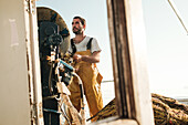 From below focused bearded male fisher in uniform seiner hunting fish with net while working on schooner in Soller near Balearic Island of Mallorca