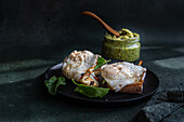 Black plate with delicious homemade wholegrain toasts with fresh green spinach, fried egg and pesto sauce placed on gray table