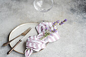Draufsicht auf arrangierte Blumen in Serviette und Gabel auf weißem Keramikteller mit Messer auf grauem Untergrund