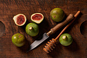 Fresh figs with a knife and honey dipper on a rustic wooden table.